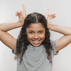 smiling-girl-making-horn-gesture-against-white-background